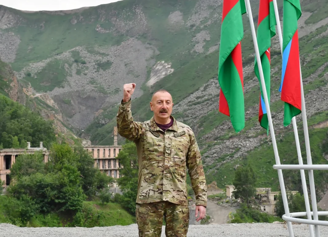 Azerbaijani President Ilham Aliyev in military uniform beside Azerbaijani flags