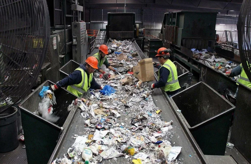 Workers sort waste on a conveyor at a processing facility