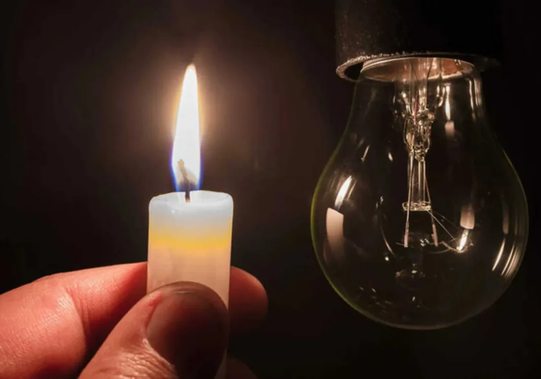 A candle burns beside an unlit light bulb during a power outage