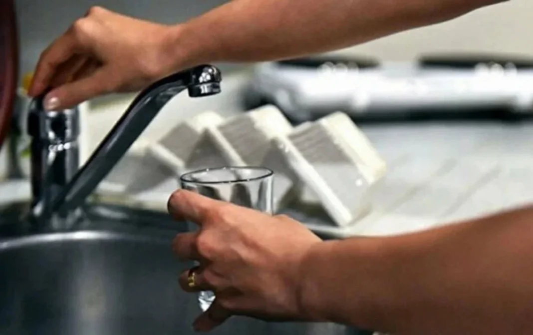 A person holds a glass under a kitchen faucet during a water supply interruption