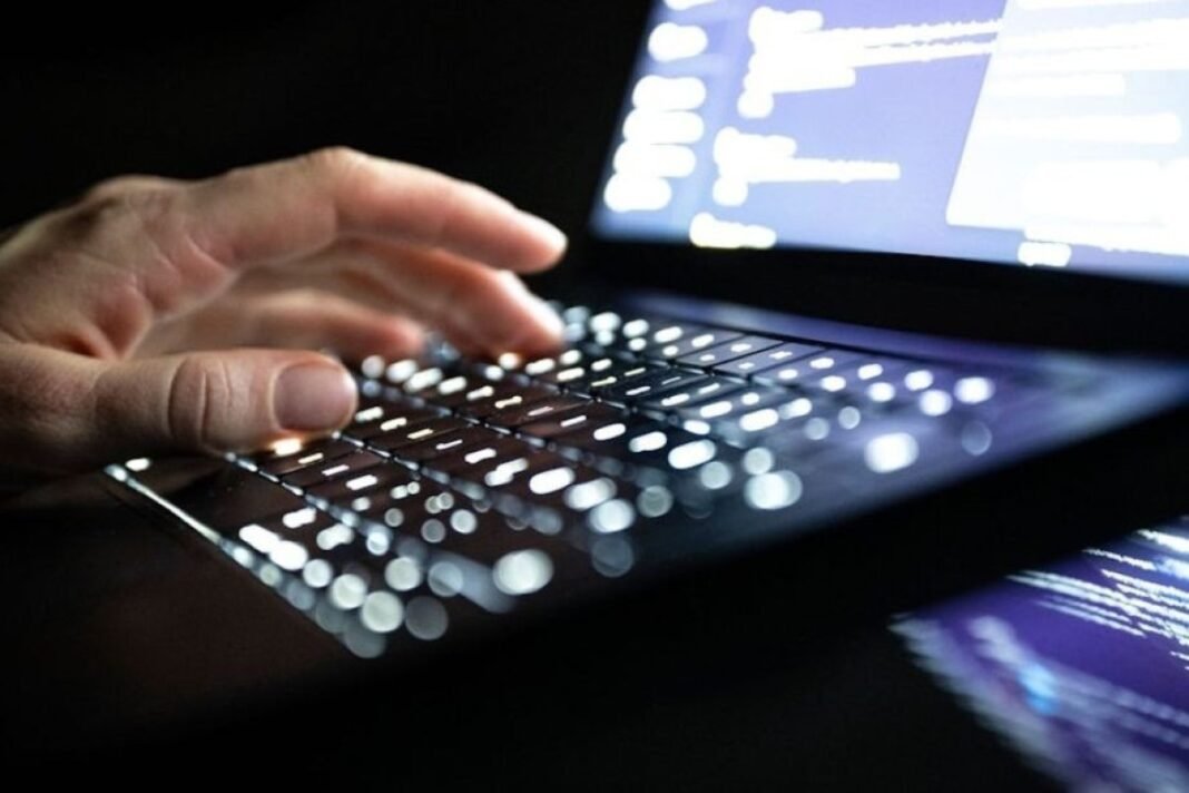 A hand over a laptop keyboard in a cybersecurity illustration.